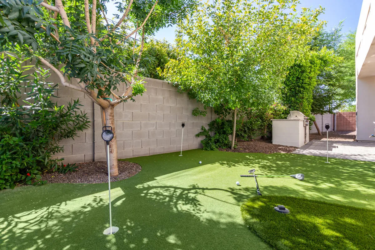 An outdoor area with lush artificial grass, garden lights, and surrounding greenery—designed for golf practice or casual games. The scene is playful yet serene and accommodates various outdoor activities.