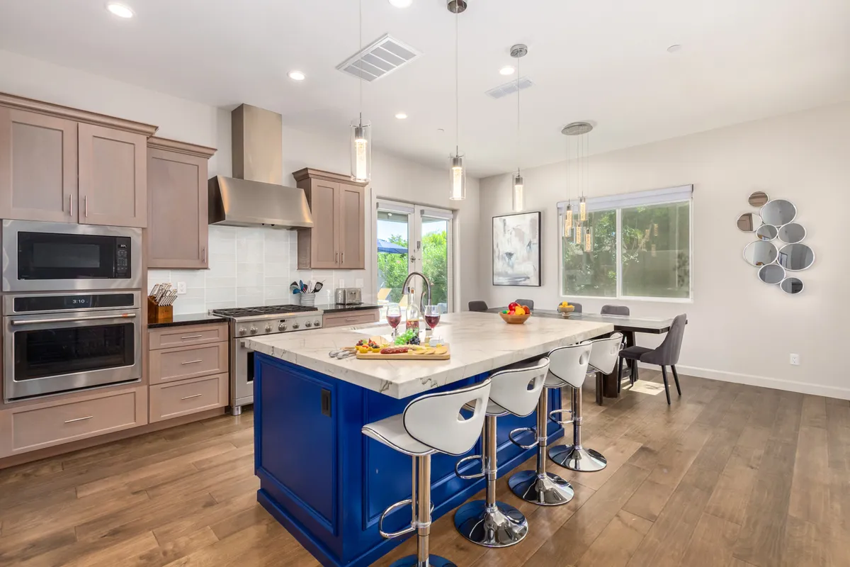 A welcoming kitchen centered around a large island with striking blue cabinetry. Stainless steel appliances, stylish pendant lights, and a gathering area with seating set the stage for family cooking sessions or entertaining guests. The space radiates warmth and functionality, ideal for culinary creativity.