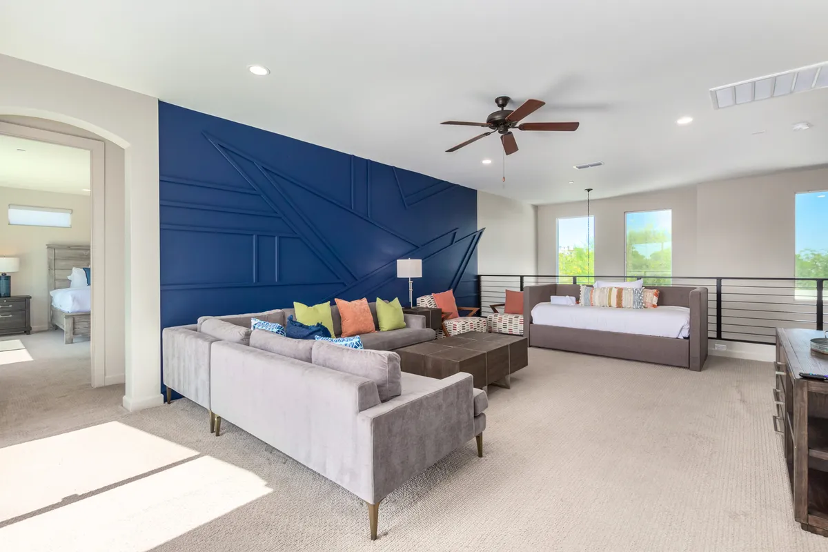 A stylish secondary living space featuring a navy blue accent wall, a comfortable sofa with colorful cushions, a daybed, and large windows flooding the room with natural light. The space feels intimate, ideal for smaller groups to enjoy conversation or a movie night.