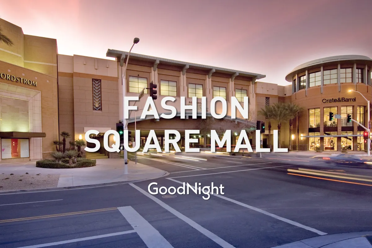 The image shows the vibrant exterior entrance to a high-end shopping mall, featuring Nordstrom and Crate & Barrel storefronts lit up in the evening. Pedestrians can be seen strolling past the illuminated shops, and the general atmosphere is lively and inviting.