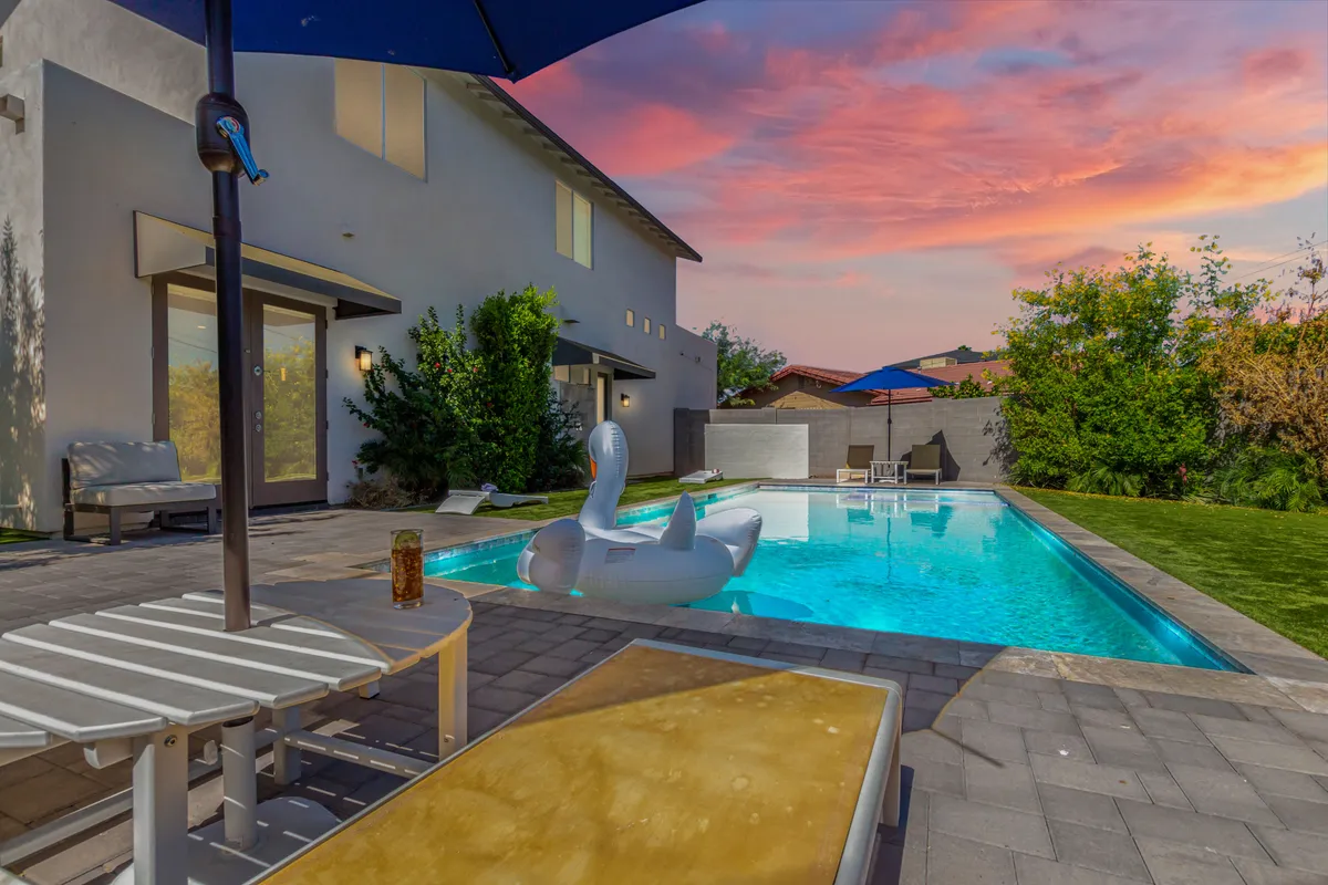 A sparkling swimming pool, floating swan, and inviting lounge chairs are surrounded by lush greenery and an outdoor umbrella. The tranquil, playful atmosphere invites relaxation and social gatherings after a day outdoors.