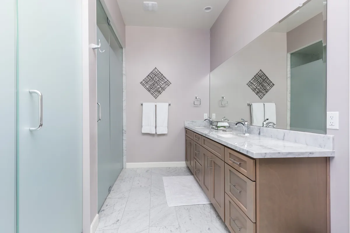 A modern bathroom with a double vanity, large mirror, glass shower door, and decorative wall art. The space exudes a spa-like feel, perfect for unwinding after a long day.