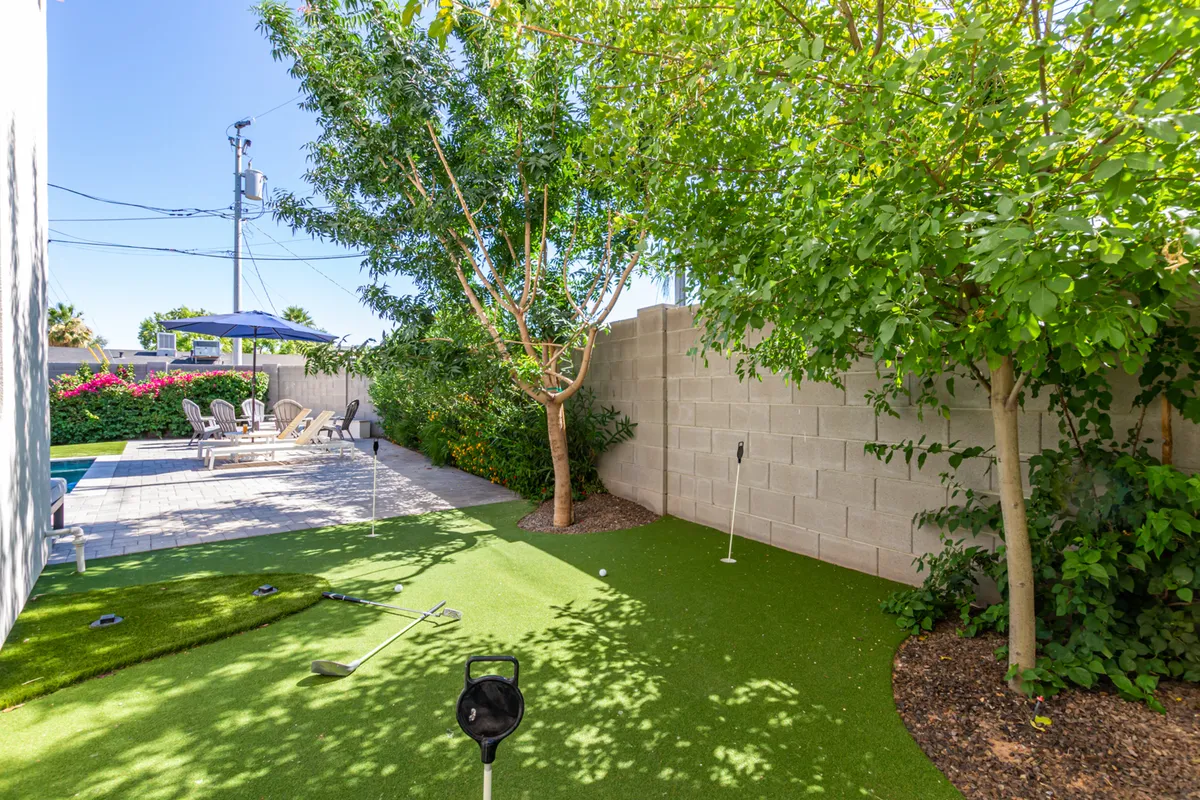 A wide exterior view of the backyard combines a lush putting green, swimming pool, and several lounge chairs. The space feels open and serene, with greenery and comfortable seating, reinforcing the oasis theme.
