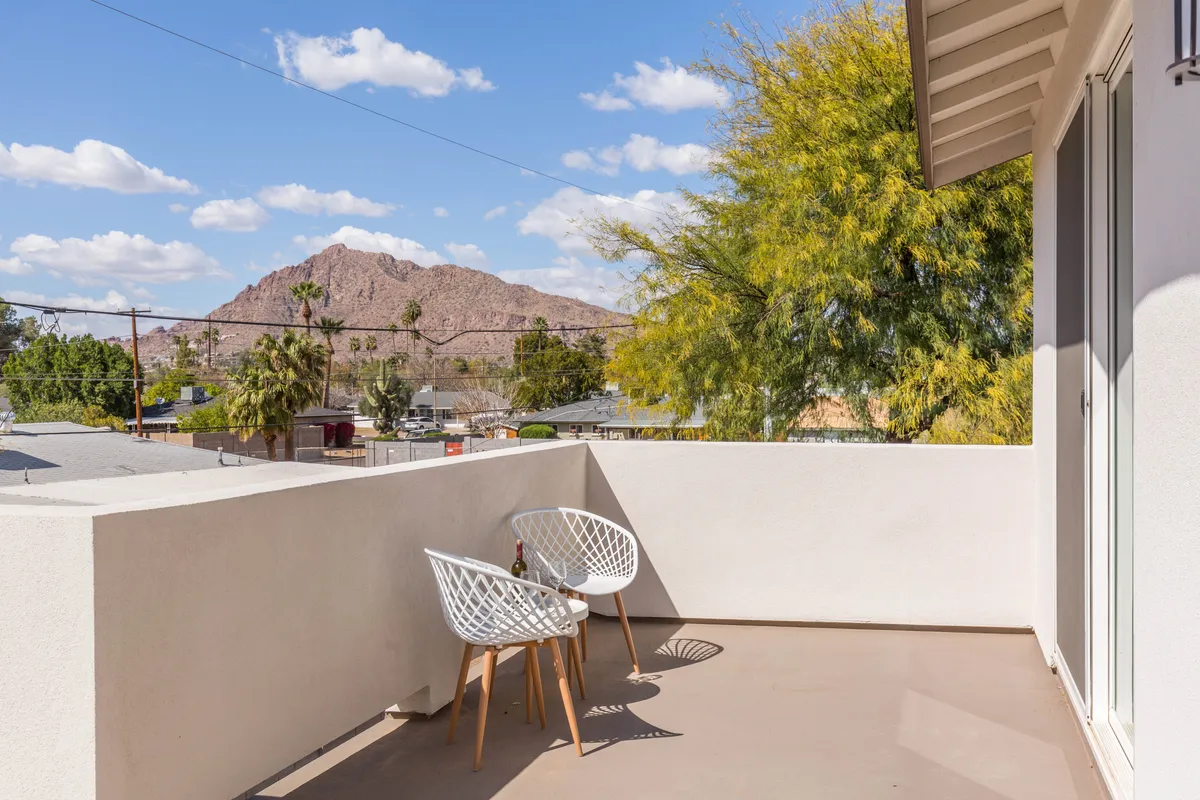 This exterior photo features a rooftop balcony with chic chairs set against a backdrop of greenery and Camelback Mountain. The elevated setting and expansive view evoke serenity and morning relaxation.